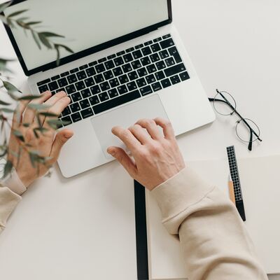 Eine Person bedient ein Notebook auf einem Schreibisch. 