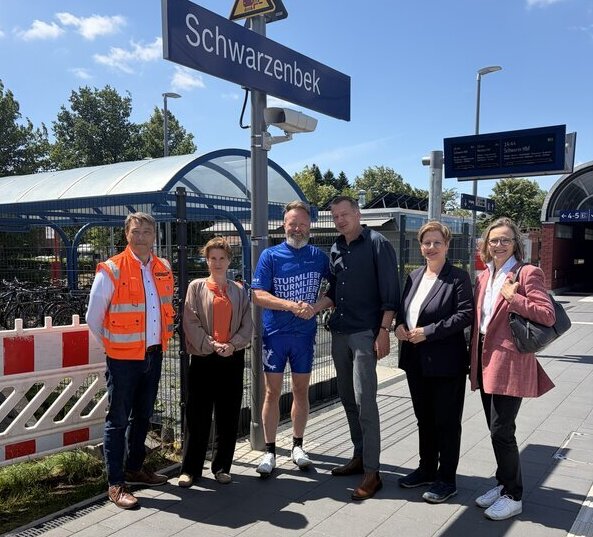 Bild vergr&ouml;&szlig;ern: Mehrere Personen stehen am Bahnsteig des Bahnhofs Schwarzenbek; Minister Madsen und B&uuml;rgermeister L&uuml;tjens begr&uuml;&szlig;en sich mit einem Handschlag.