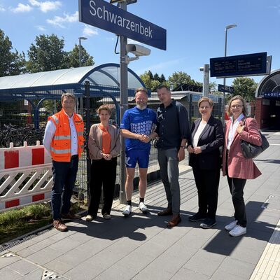 Mehrere Personen stehen am Bahnsteig des Bahnhofs Schwarzenbek; Minister Madsen und B&uuml;rgermeister L&uuml;tjens begr&uuml;&szlig;en sich mit einem Handschlag.