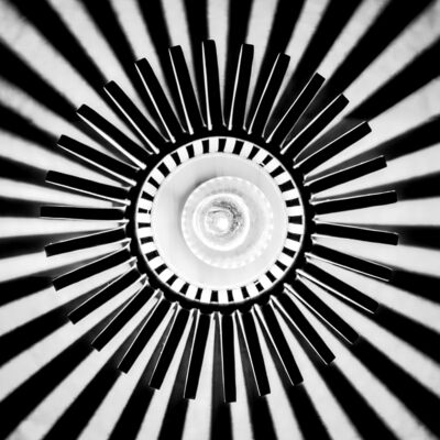 Auf dem quadratischen Bild ist ein Zusammenspiel aus schwarzen und wei&szlig;en sind abwechselnden Elementen zu sehen. Sie laufen von den R&auml;ndern des Bildes strahlenf&ouml;rmig Richtung Mitte des Bildes, laufen aber nicht in der Mitte zusammen, sondern enden in einem schwarzen Kreis. Innerhalb des Kreises ist es vorwiegend wei&szlig;. Die Interpretation des Abgebildeten obliegt dem Betrachtenden.
