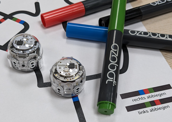 Bild vergr&ouml;&szlig;ern: Das Bild zeigt zwei Ozobot-Roboter neben denen farbige Stifte liegen.