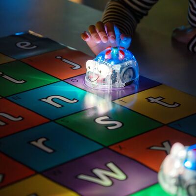 Leuchtende Beebots fahren &uuml;ber einen bunten Untergrund mit Buchstaben.